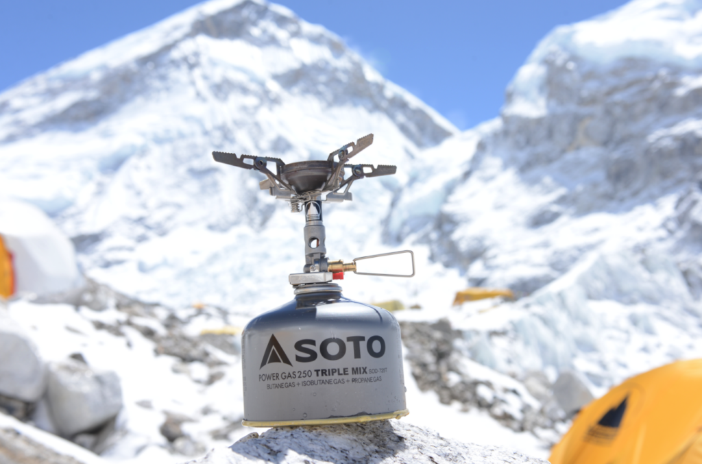 BaAckpacking stove with fuel canister at a high-altitude campsite in a snowy mountain environment, illustrating fuel needs for backpacking trips
